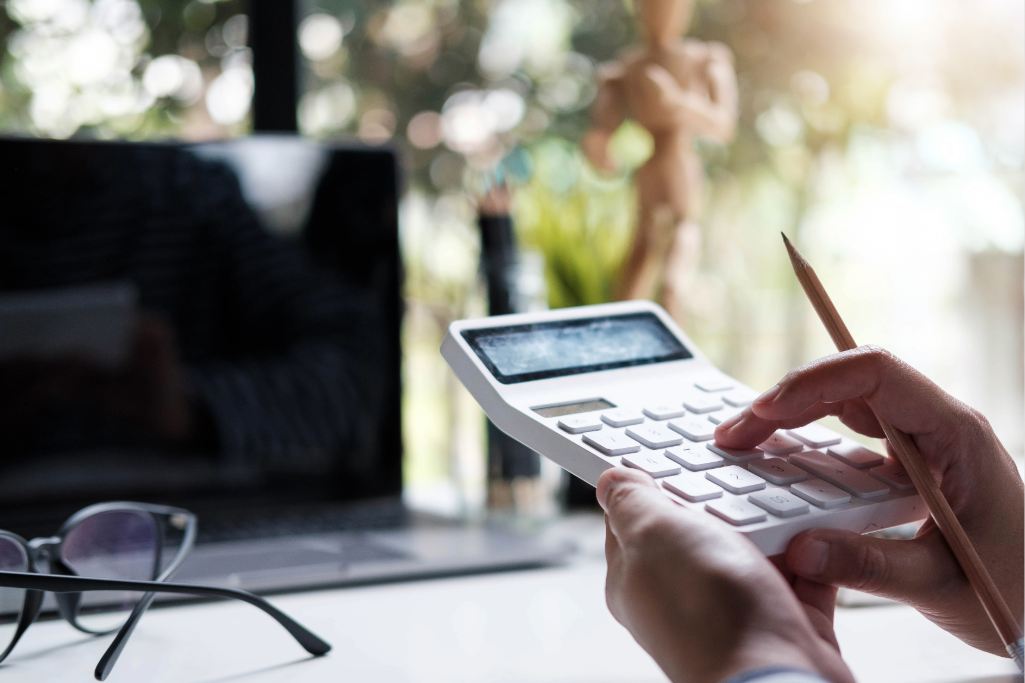 Mãos operando calculadora branca e segurando lápis à frente de notebook. Passo a passo de como calcular qualidade de segurado e tempo de contribuição.