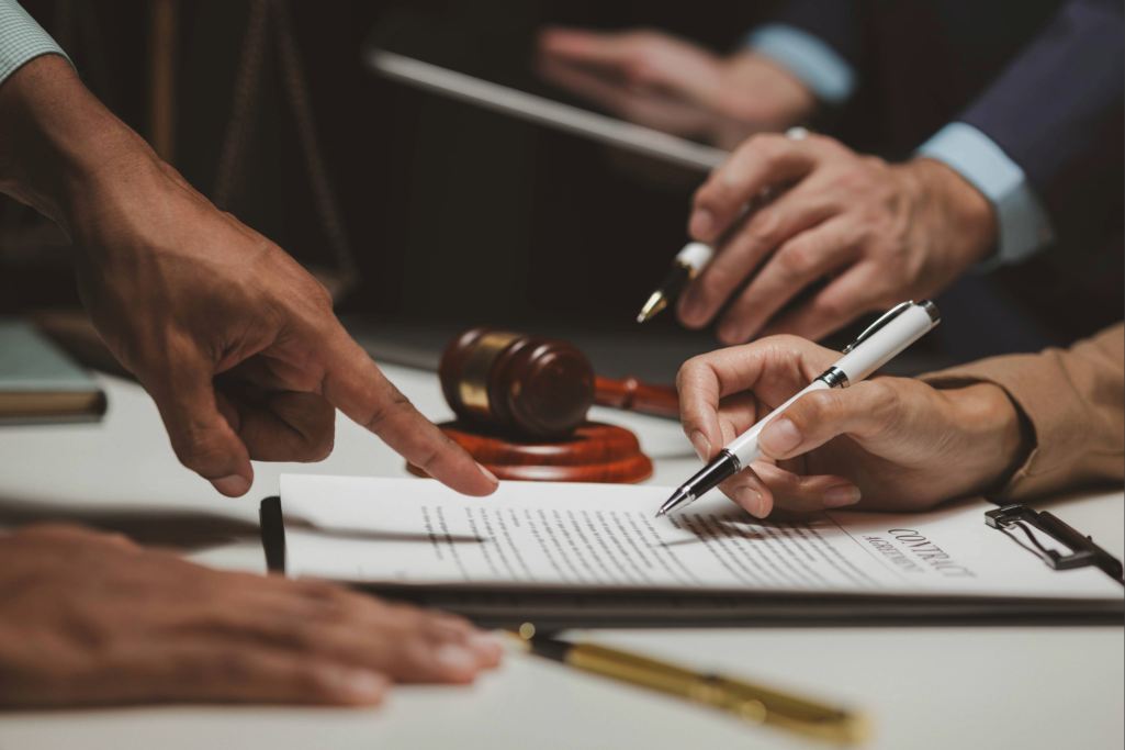 Mão apontando para cláusulas de um contrato sobre mesa com martelo de juiz ao fundo. Segurança jurídica garantida pelo direito adquirido.