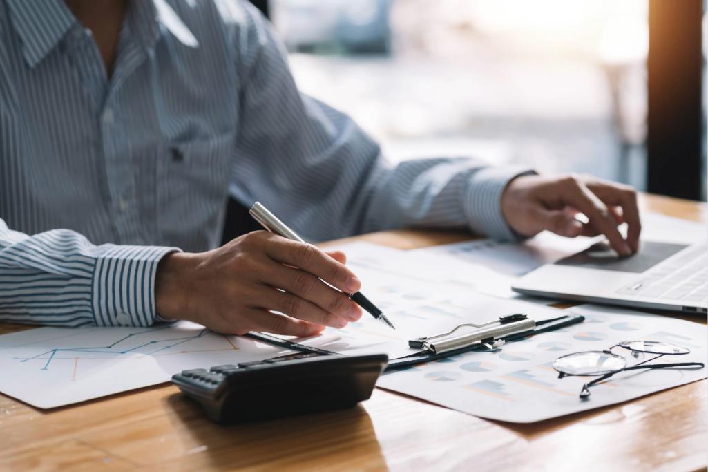 Homem analisando relatórios estatísticos com calculadora e notebook. Verificação de carência para qualidade de segurado em benefícios por incapacidade.